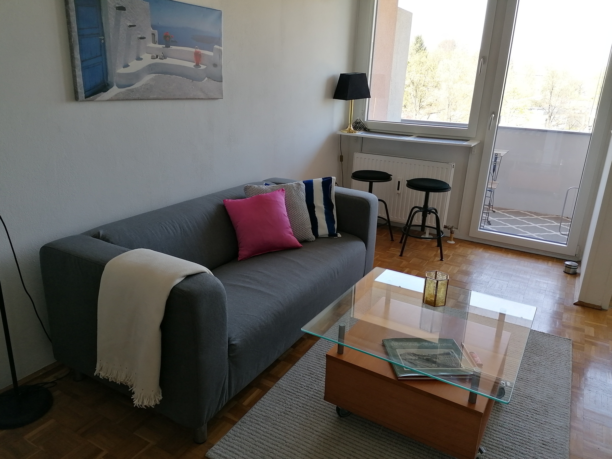 Wohnraum, ausgestattet mit einer Couch, einem Tisch, Theke am Fenster mit 2 Hockern, Schubladkasten, großer Kleiderschrank und einer Schlafnische mit einem Bett 140x200